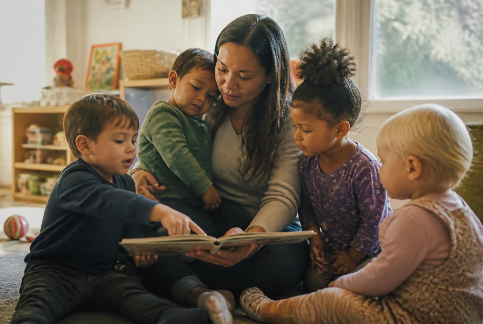 A family home daycare provider sharing a story with four children gathered close